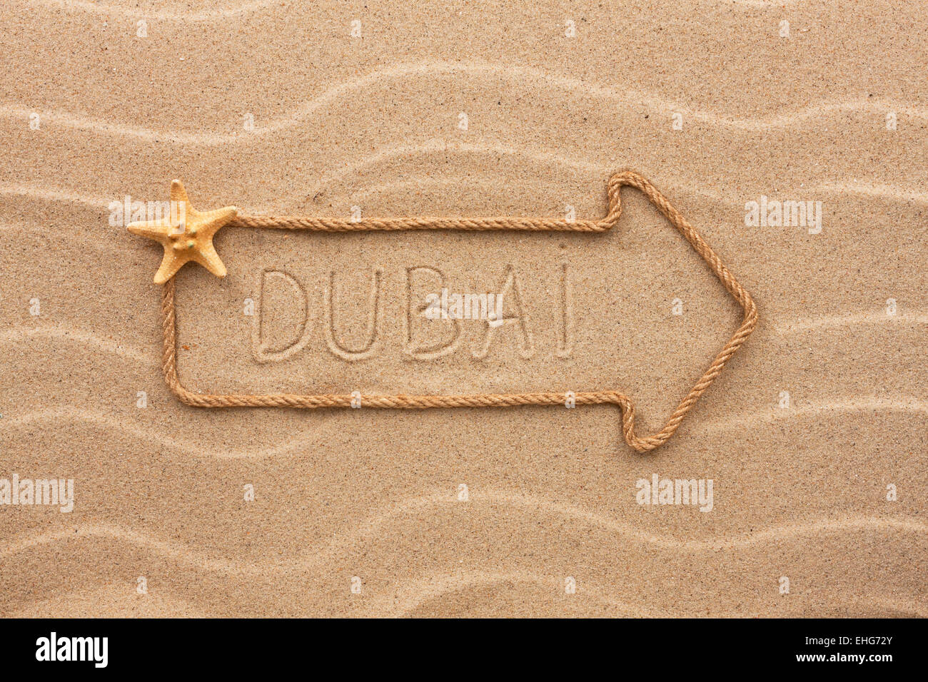 Freccia fatta di corda e conchiglie di mare con la parola Dubai sulla sabbia, come sfondo Foto Stock