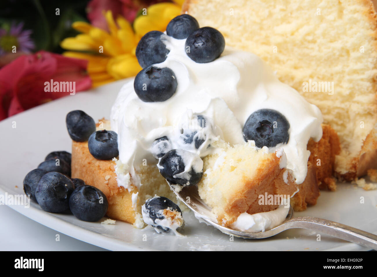 Fetta di ciambellone con panna montata e rabboccato con mirtilli e fiori in background Foto Stock