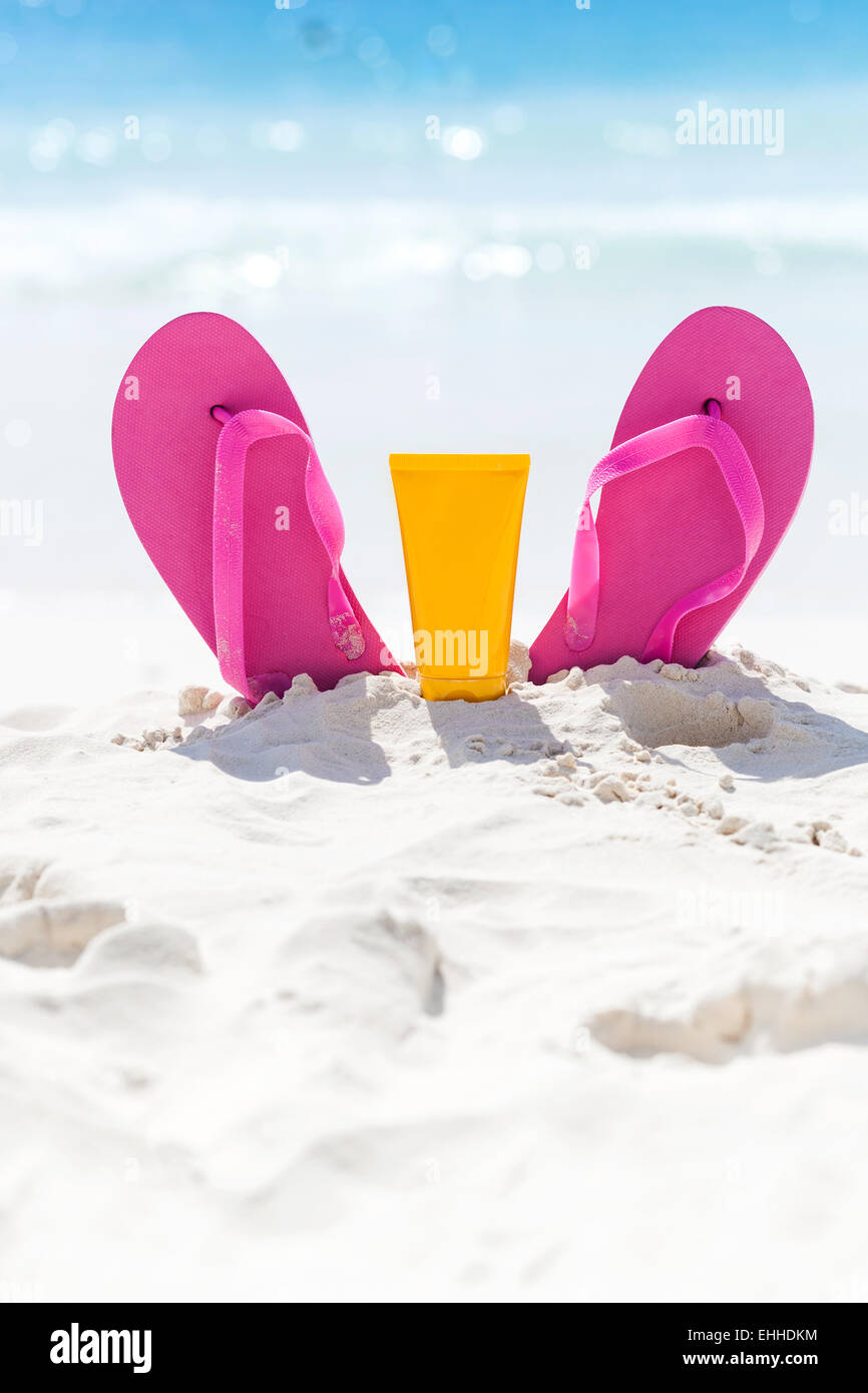 Rosa vivace spiaggia flip flop con protezione solare Crema per il viso in sabbia bianca su sfondo del mare. Tropical vacanze estive con Foto Stock