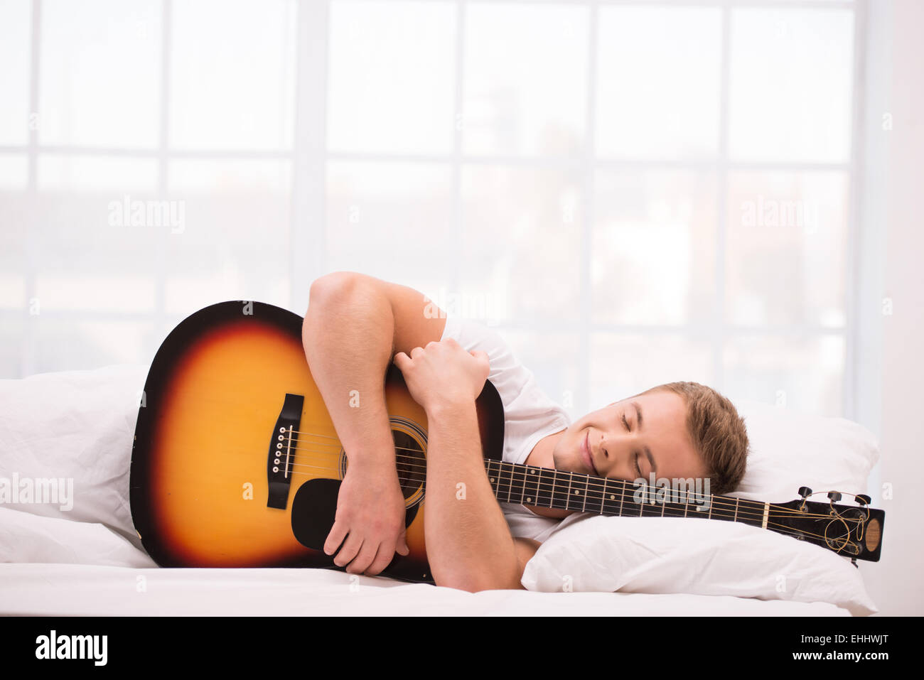 Giovane uomo disteso nel letto con la chitarra Foto Stock