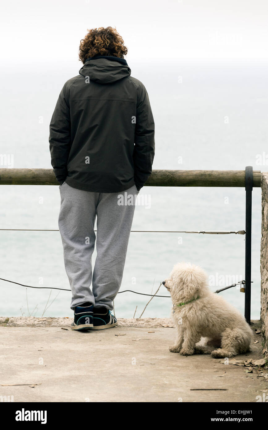 SANTANDER, Spagna - 11 Marzo 2015: un giovane uomo e il suo cane che guarda verso il mare su una mattina di inverno Foto Stock