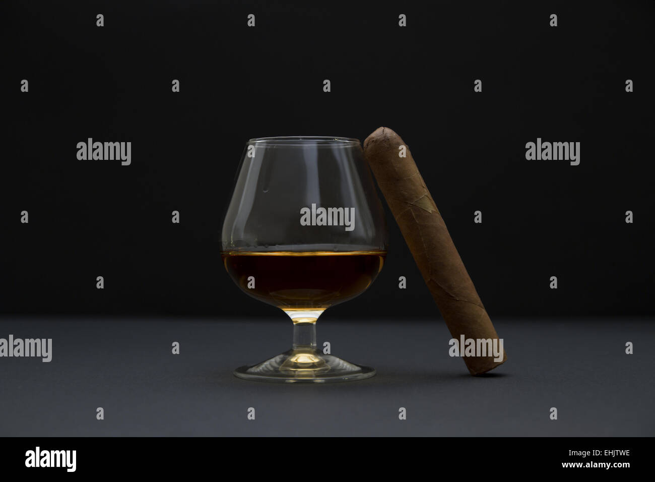 Vista laterale di un robusto dimensionato sigaro e un bicchiere di cognac. Lo sfondo scuro e la profondità di campo. Foto Stock