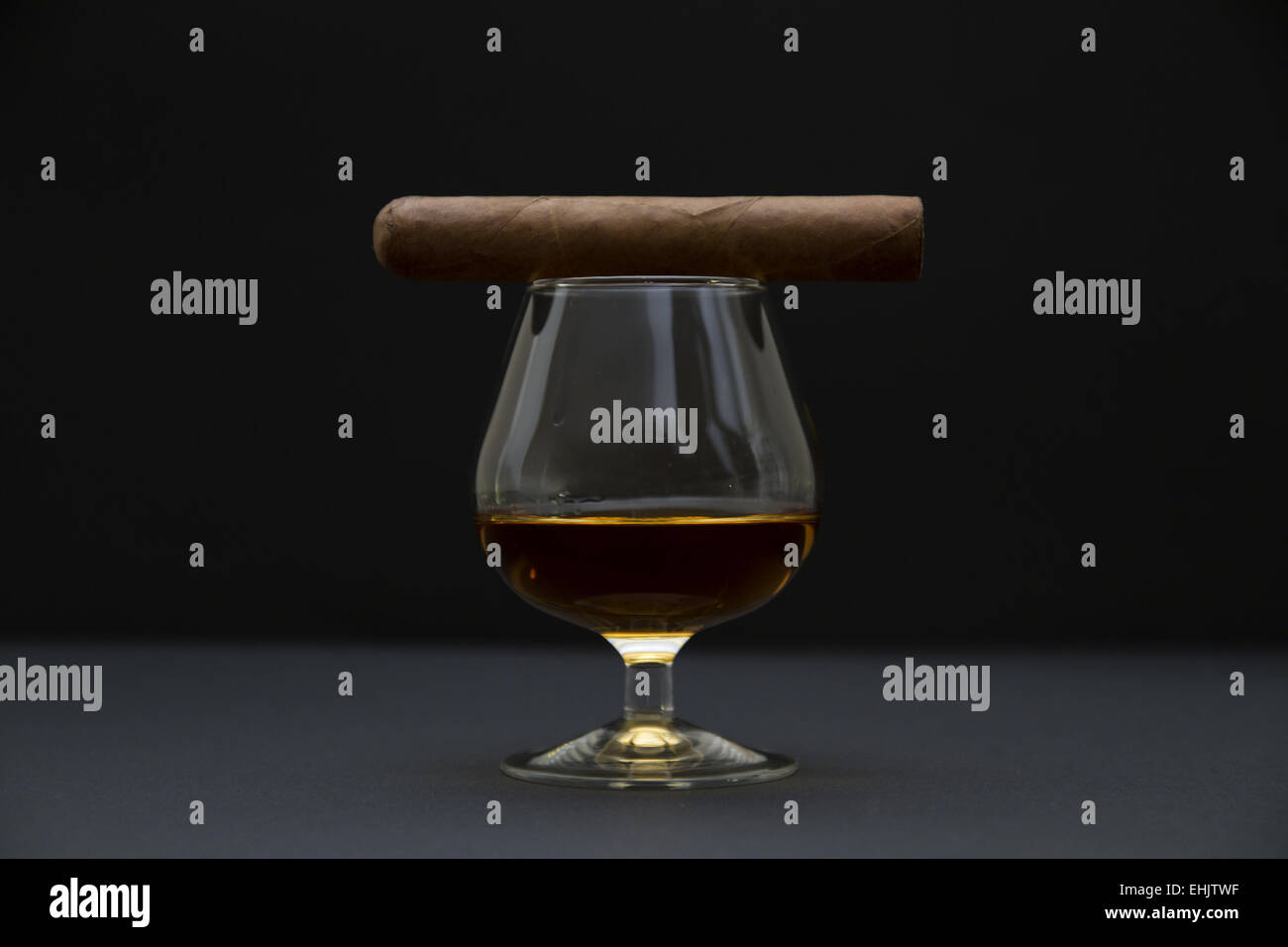 Vista laterale di un robusto dimensionato sigaro e un bicchiere di cognac. Lo sfondo scuro e la profondità di campo. Foto Stock