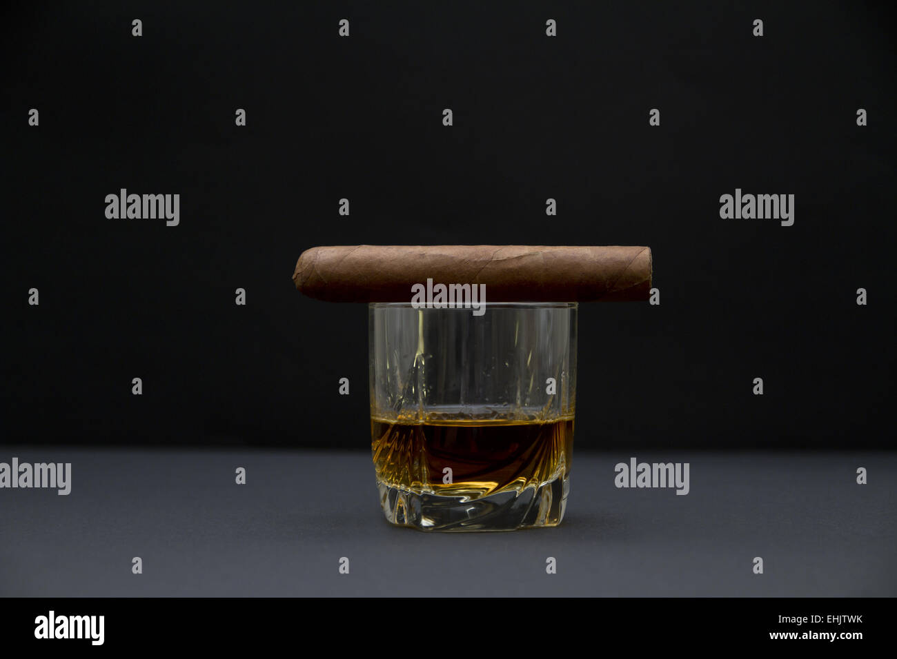 Vista laterale di un robusto dimensionato sigaro e un bicchiere di Whiskey. Lo sfondo scuro e la profondità di campo. Foto Stock