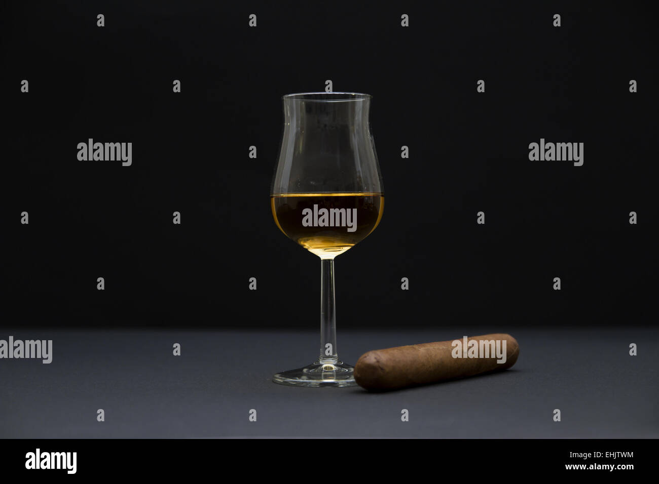 Vista laterale di un robusto dimensionato sigaro e un bicchiere di cognac. Lo sfondo scuro e la profondità di campo. Foto Stock