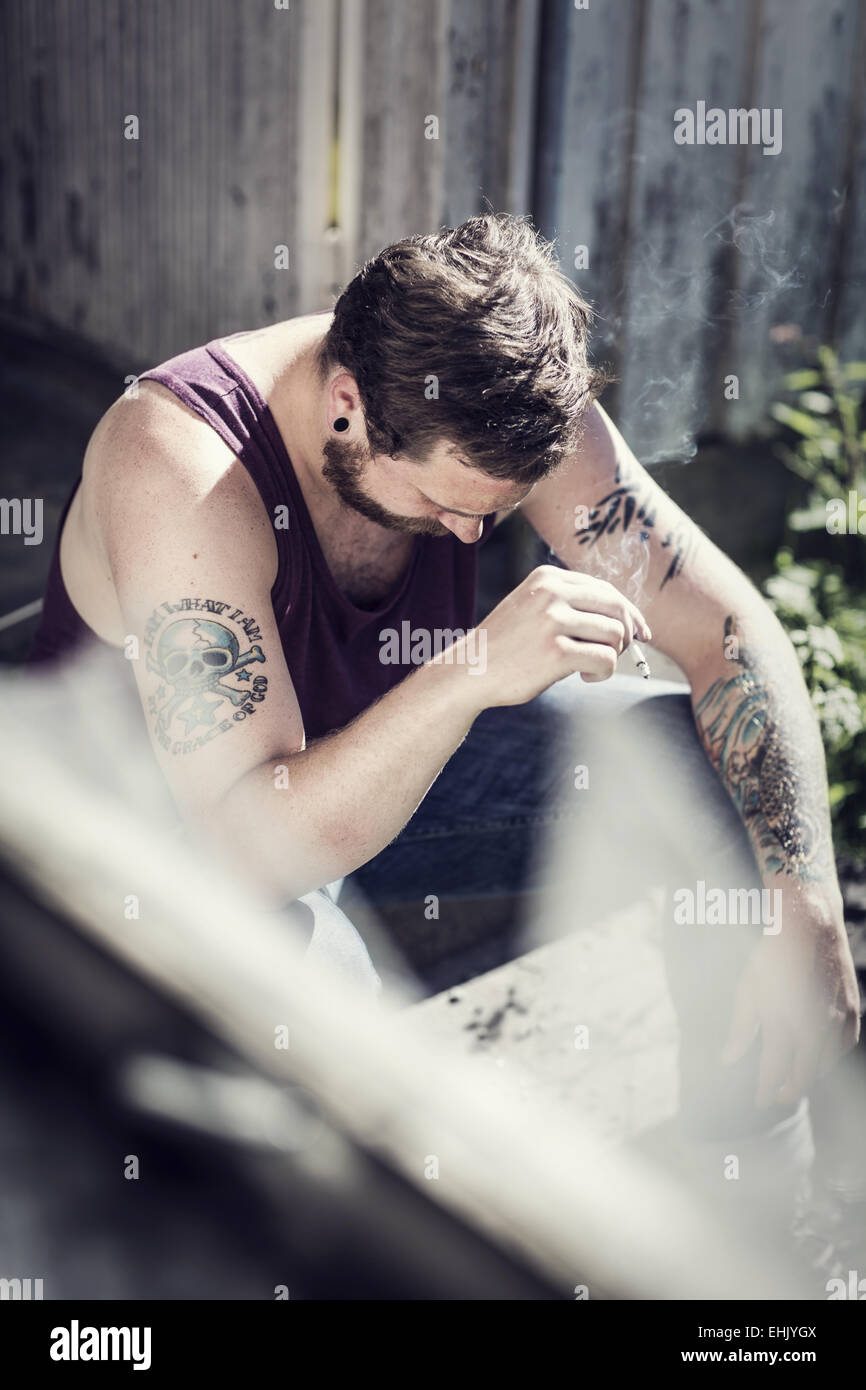 Un redneck seduta al di fuori di una casa abbandonata e fumo di sigarette. Foto Stock