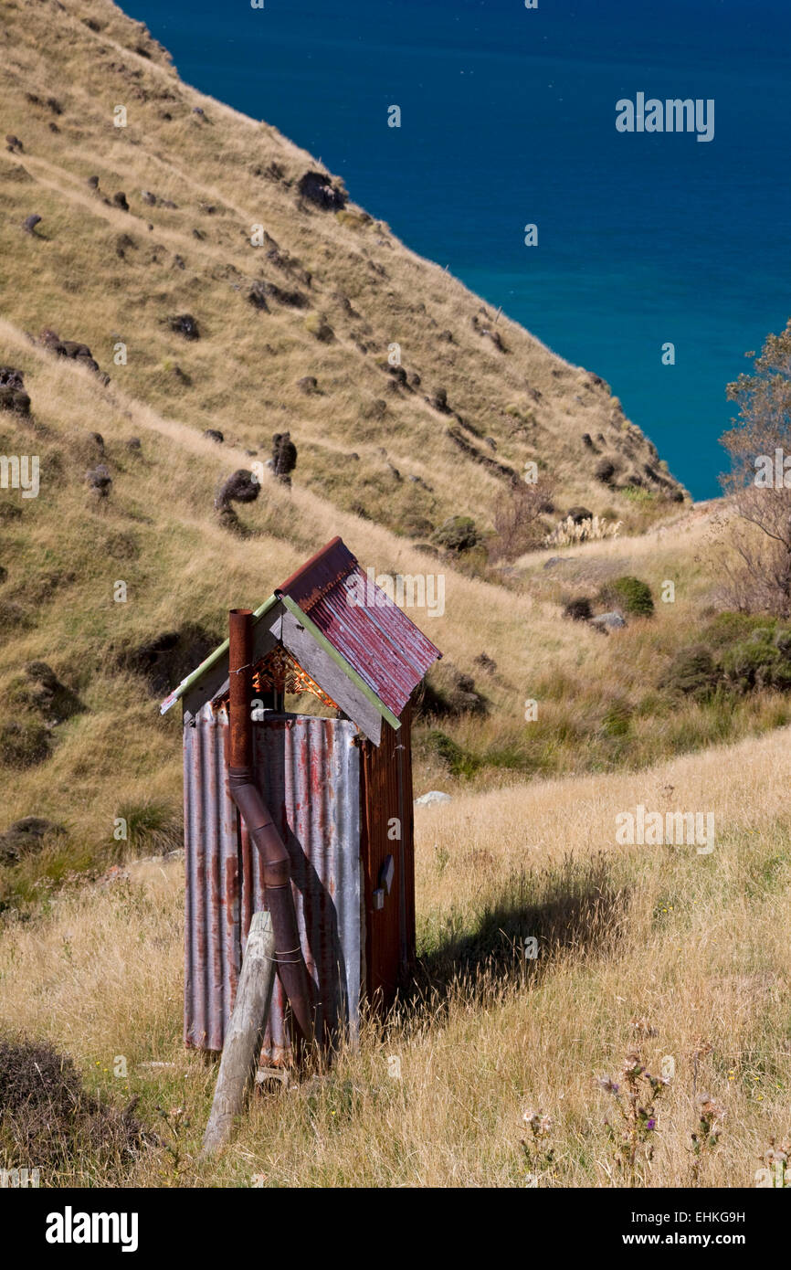Un metallo ondulato dipendenza privato wc sul pendio di una collina con una vista sulla Penisola di Banks via, Nuova Zelanda, Isola del Sud Foto Stock