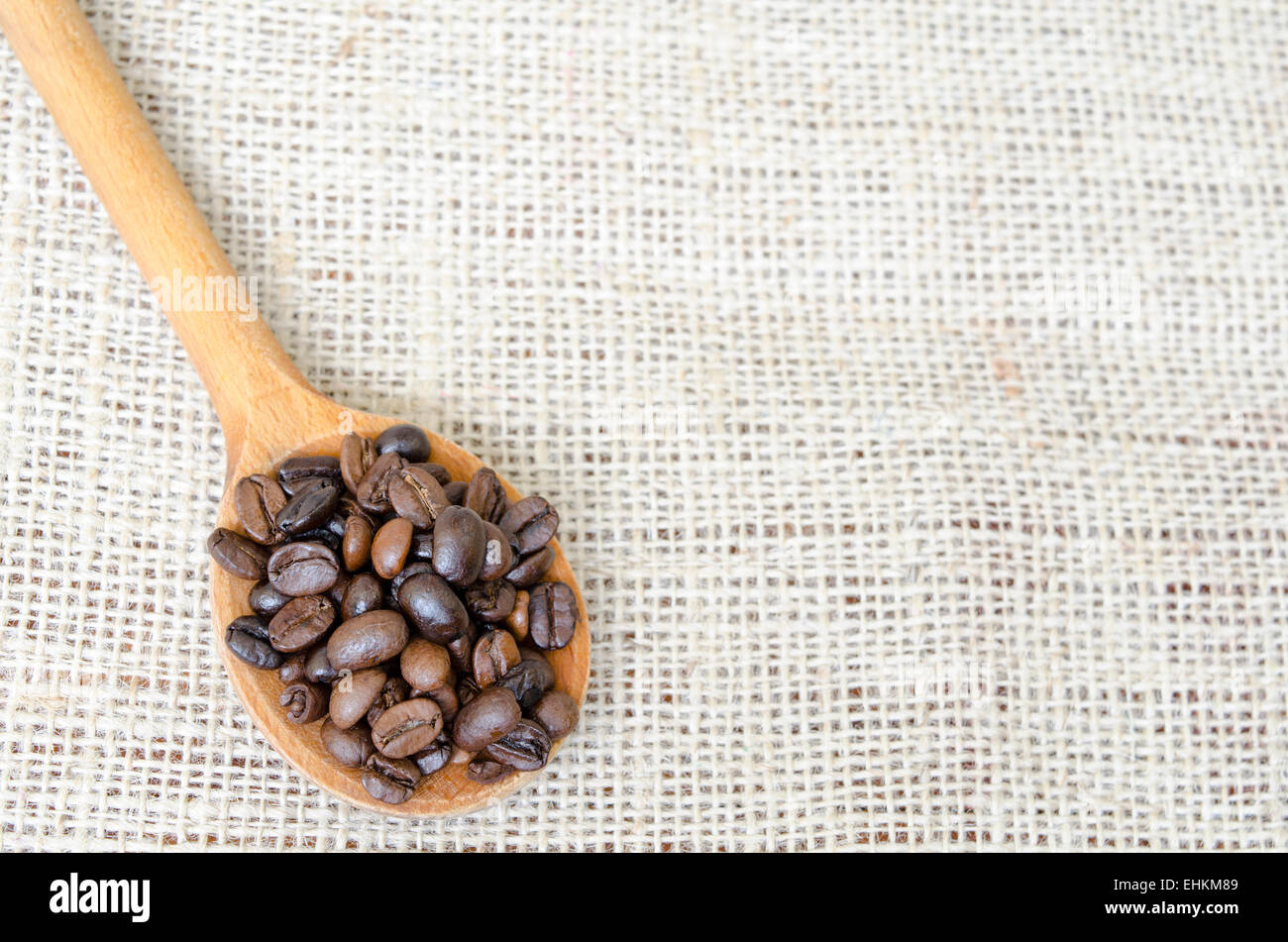 Cucchiaio di legno pieno con chicchi di caffè tostati su una tovaglia vintage Foto Stock