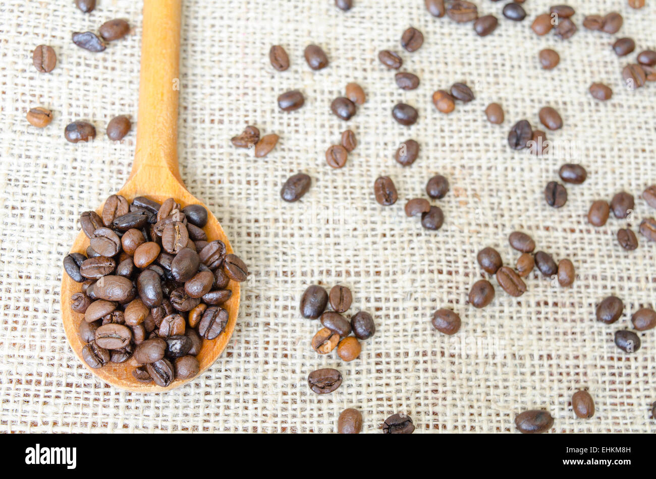 Cucchiaio di legno pieno con chicchi di caffè tostati su una tovaglia vintage Foto Stock
