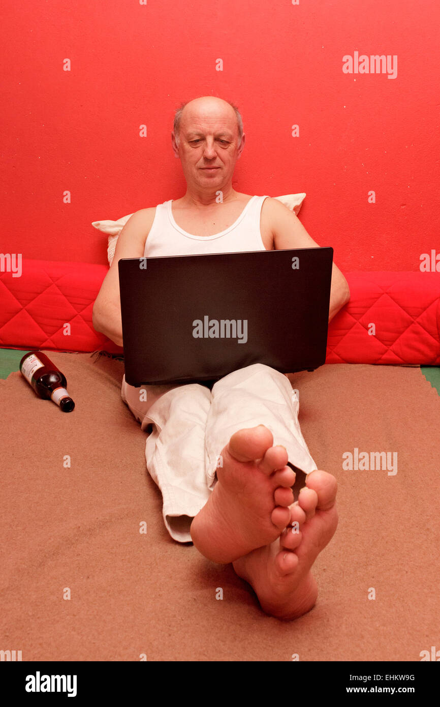Uomo seduto nel suo letto con il suo computer portatile sul suo giro Foto Stock