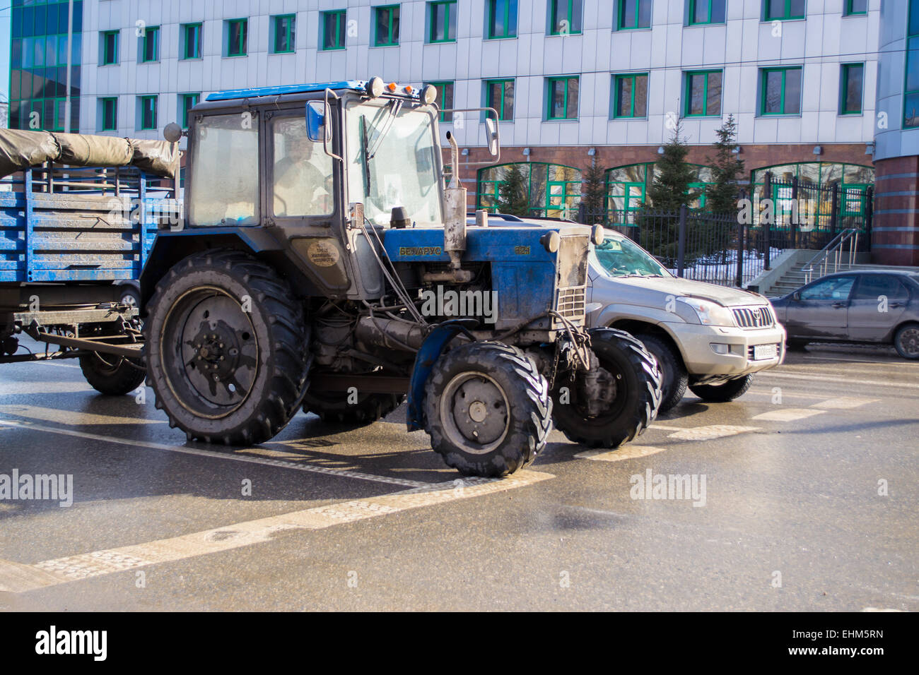 Un vecchio trattore blu diventa pronto per la gara di un moderno su una macchina high street in Russia durante la giornata nel centro della città Foto Stock