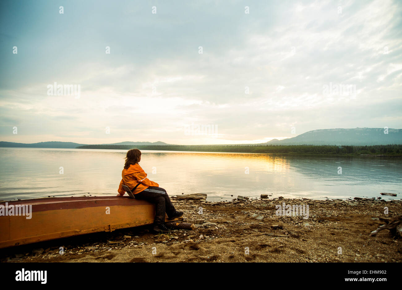 Caucasian donna seduta su fatiscente barca al lago rurale Foto Stock