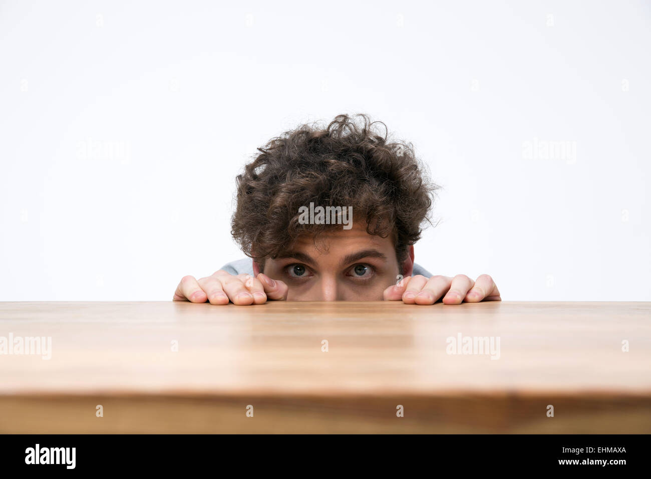 Giovane uomo con capelli ricci spiata da dietro la scrivania Foto Stock