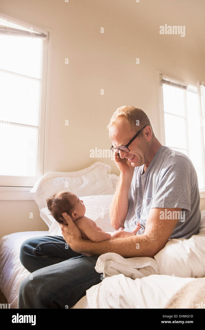 Padre parlando al cellulare e trattenere il bambino sul letto Foto Stock