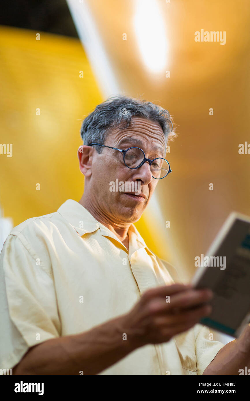 Vecchio uomo caucasico la lettura di libro in biblioteca Foto Stock