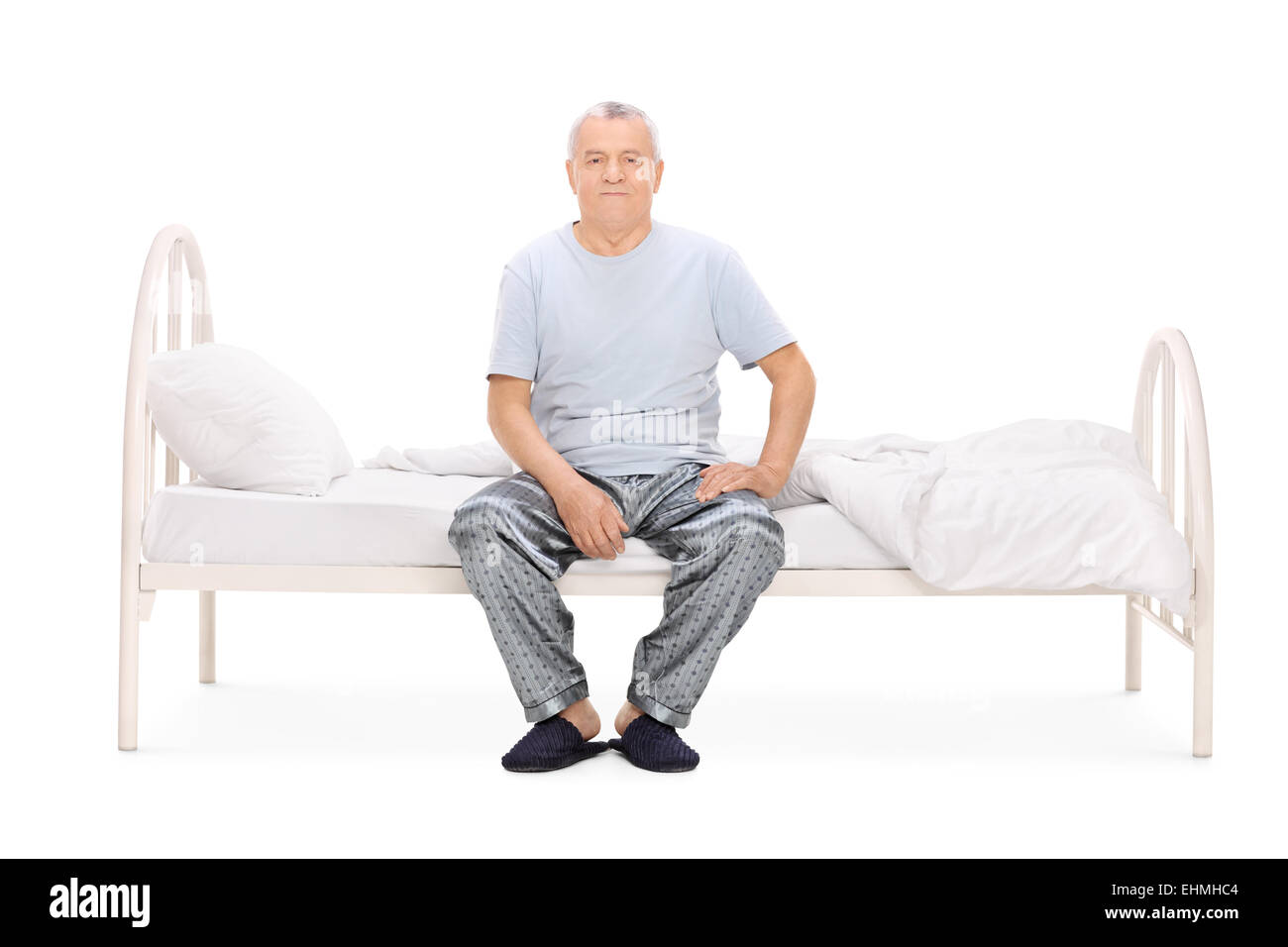 Senior uomo in pigiama seduto su un letto isolato su sfondo bianco Foto Stock