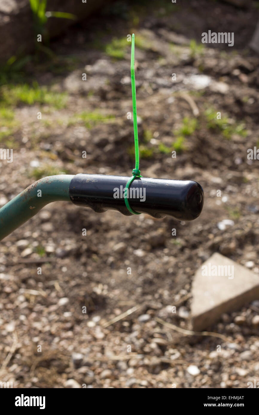 Fascetta serracavi verde o impianto cravatta attorno ad una carriola nero maniglia Foto Stock