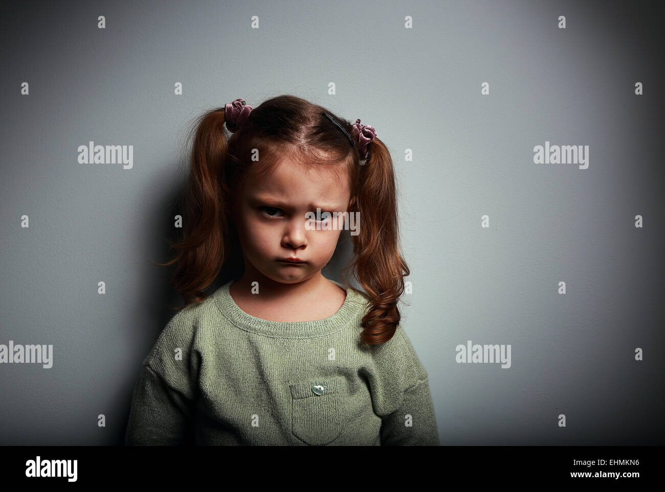 Triste kid ragazza guarda con molto infelice faccia su sfondo scuro Foto Stock