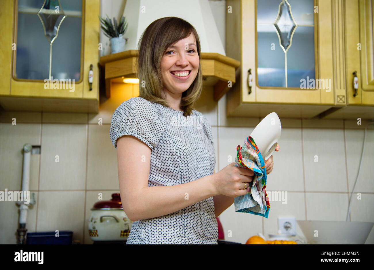 Donna sorridente tergi una piastra in cucina Foto Stock