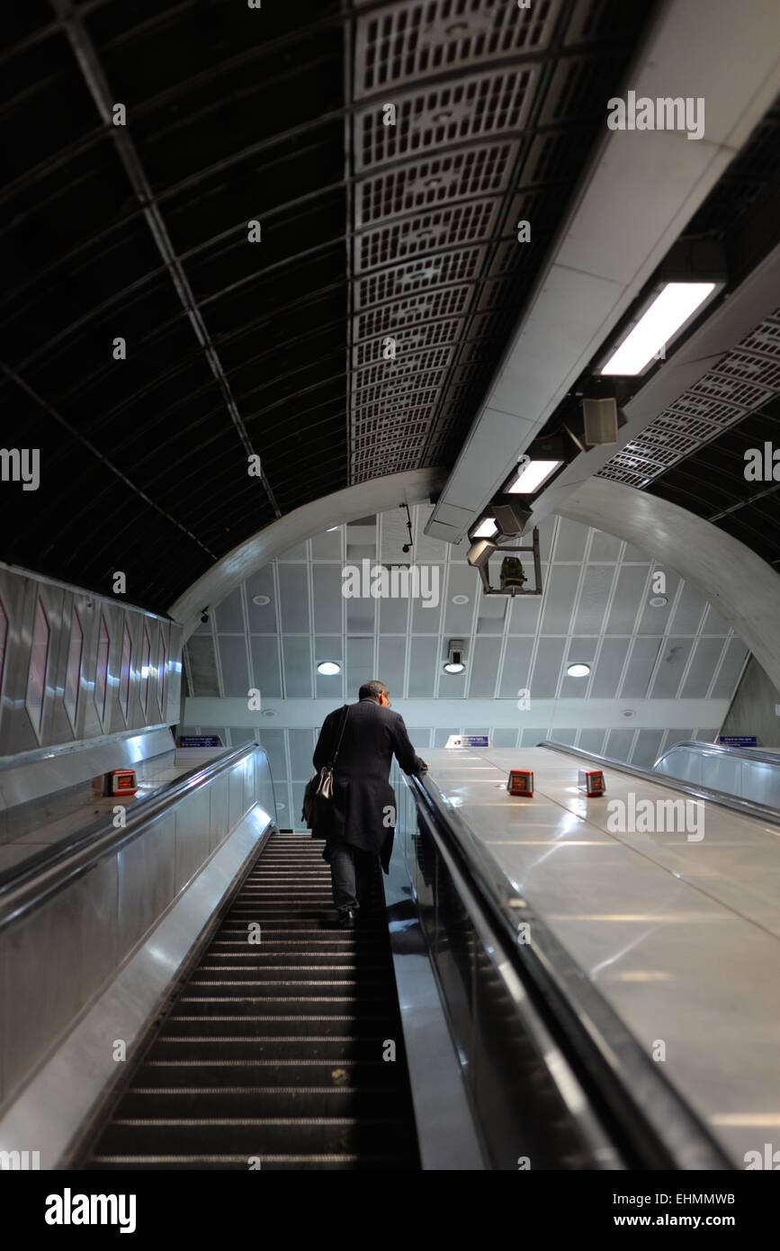Un uomo che sale su una scala mobile in una stazione della metropolitana di Londra Foto Stock