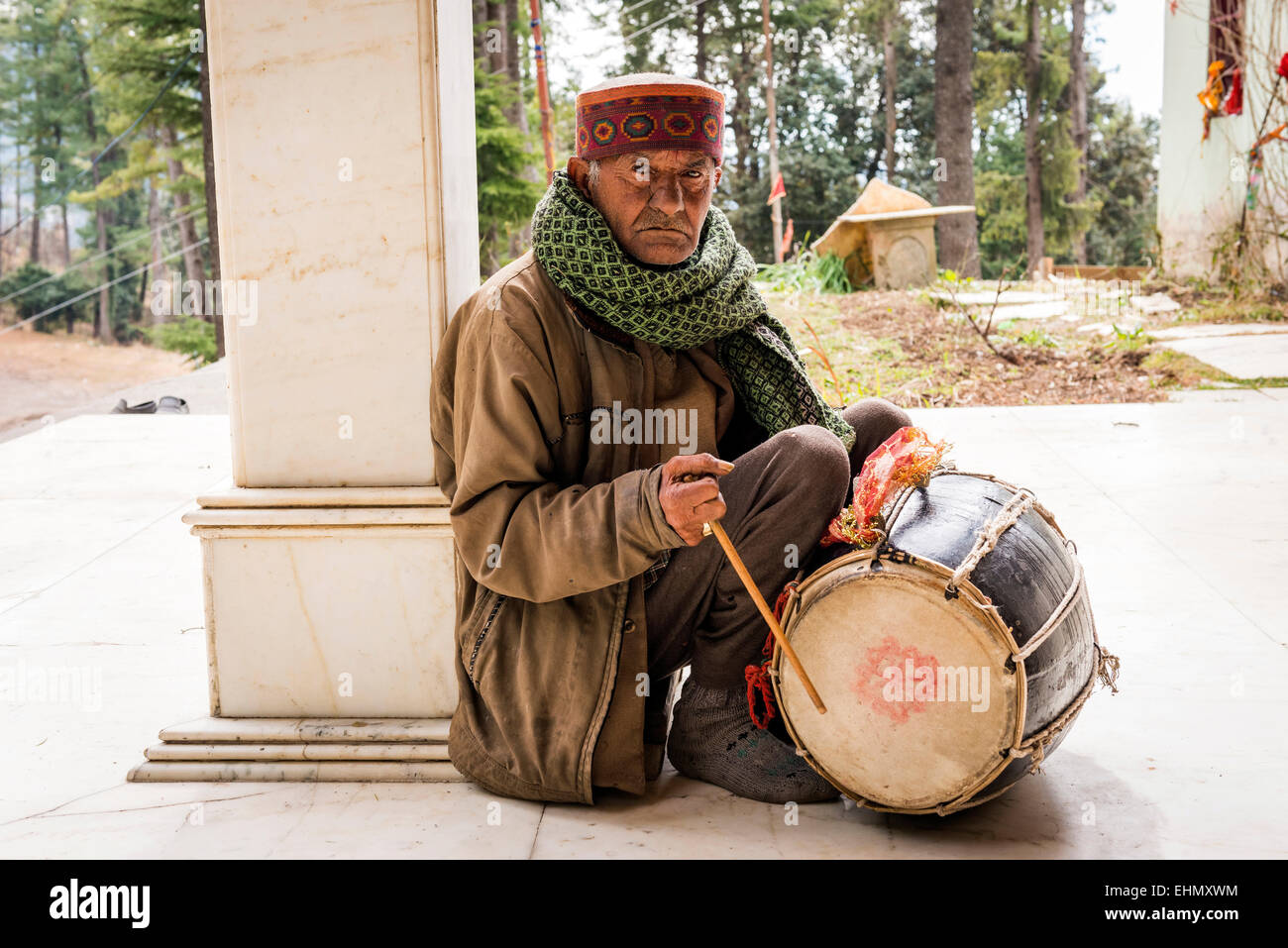 Il vecchio uomo indù con un tamburo al di fuori di un piccolo tempio in collina nei pressi di Shimla, Himachal Pradesh, India Foto Stock