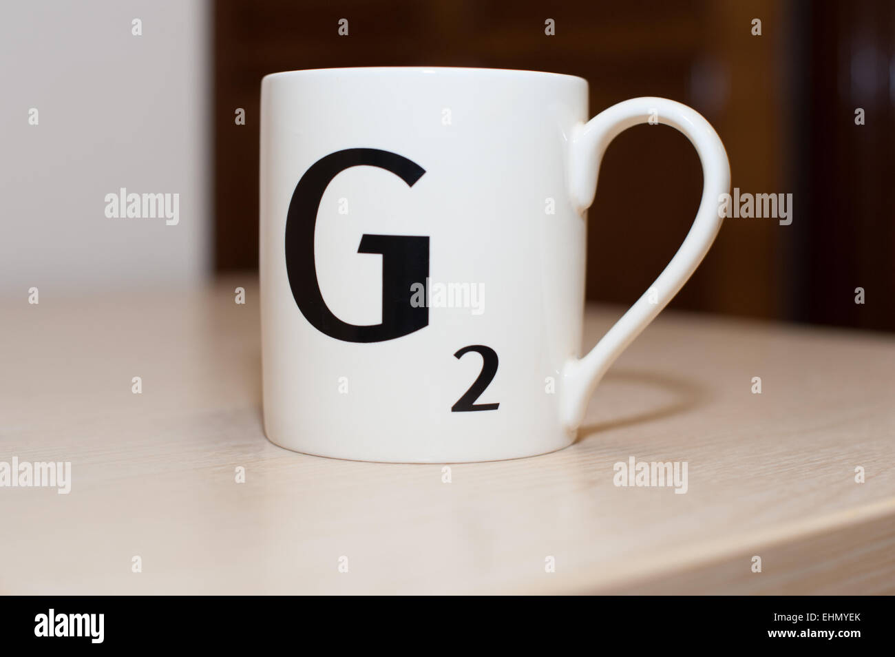 Una lettera di scrabble , un capitale g con due punti su una bianca la tazza di tè o caffè durante una pausa di lavoro su un tavolo Foto Stock