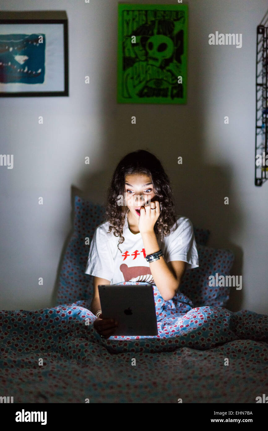 Ragazza adolescente utilizzando una tavoletta digitale di notte. Foto Stock