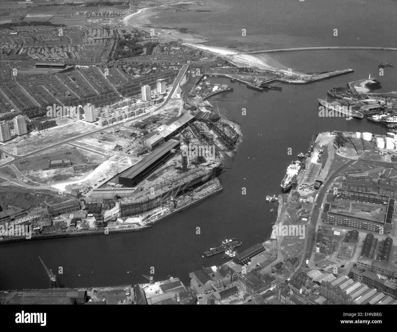 Questa fotografia aerea, scattata nel 1964, cattura il cantiere navale di North Sands a Sunderland, Regno Unito. Mostra le operazioni di costruzione navale lungo il fiume Wear, con la chiesa di San Pietro e Roker Park sullo sfondo. Il cantiere navale fu un sito chiave per la costruzione navale britannica durante il XX secolo. Foto Stock