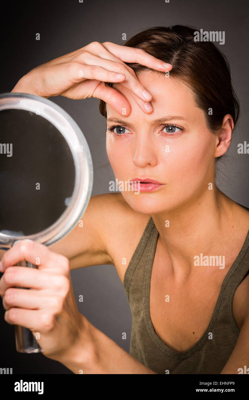 Donna controllando la sua faccia nello specchio. Foto Stock