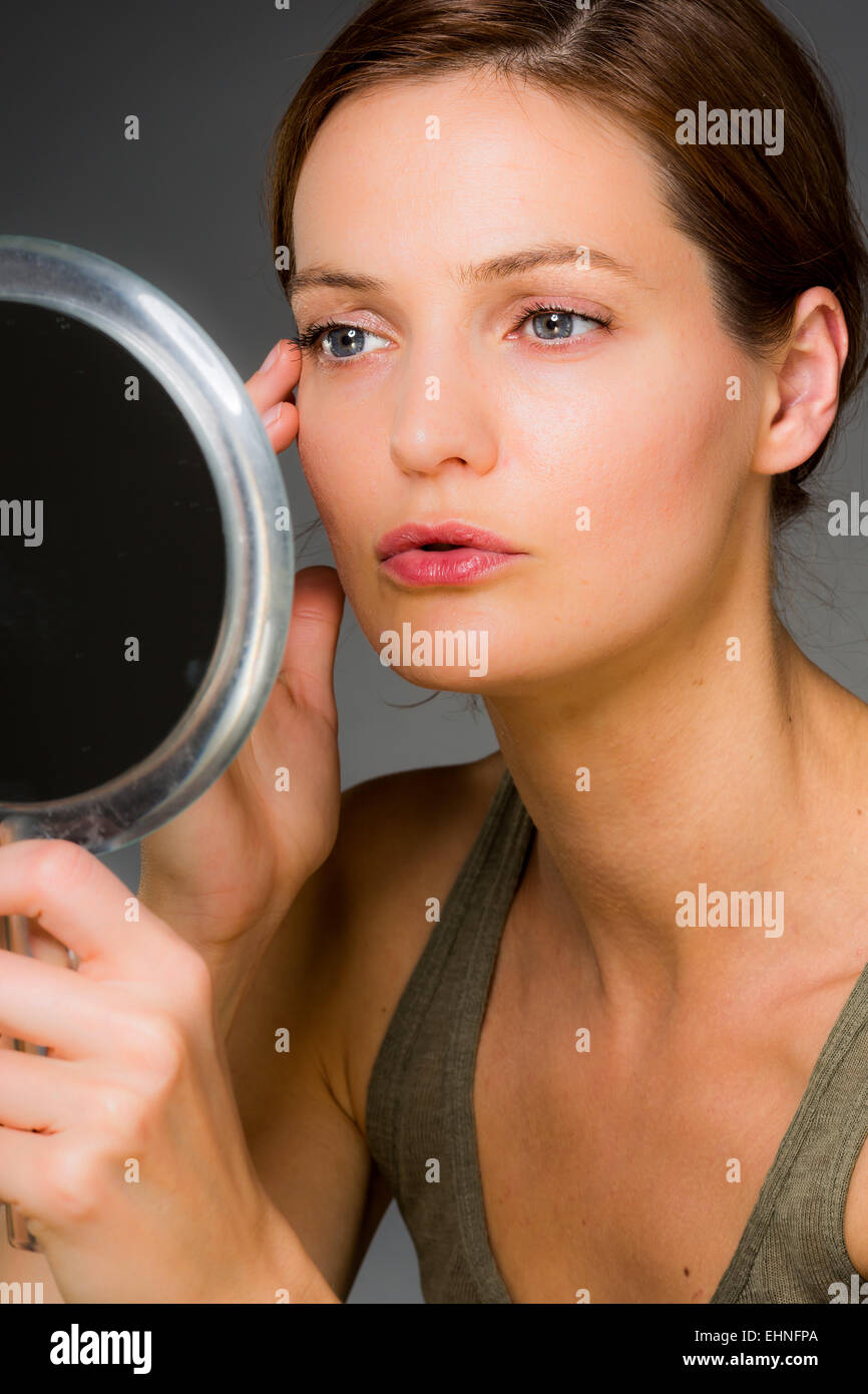 Donna controllando la sua faccia nello specchio. Foto Stock