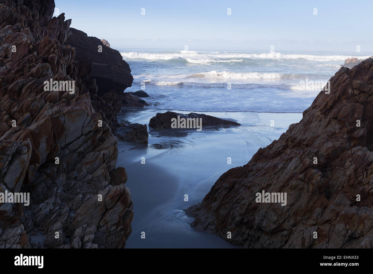 Rotolo di onde in spiaggia tra due promontori rocciosi sulla spiaggia di Hermanus. Foto Stock