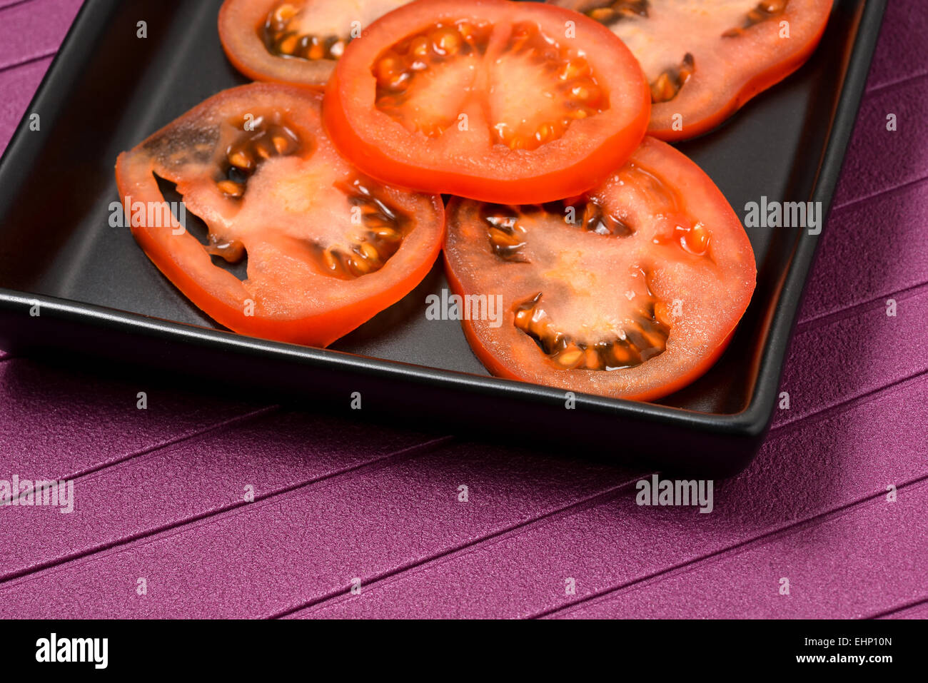 Un sacco di fettine ​​tomato disposti in un nero vaso in ceramica con sfondo viola Foto Stock