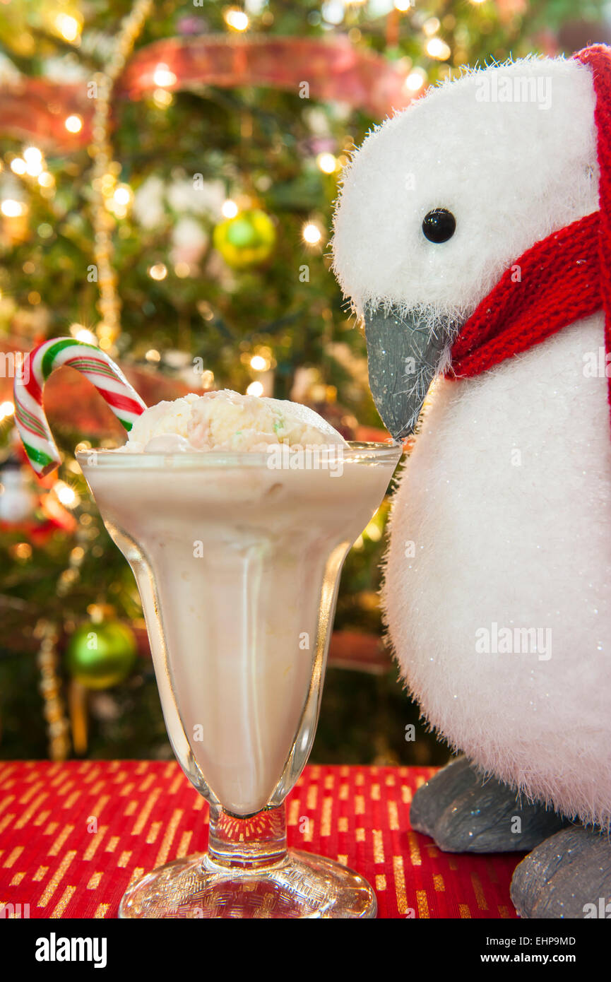 Natale penguin guarda a un piatto di candy cane gelato nella parte anteriore dell'albero di Natale Foto Stock