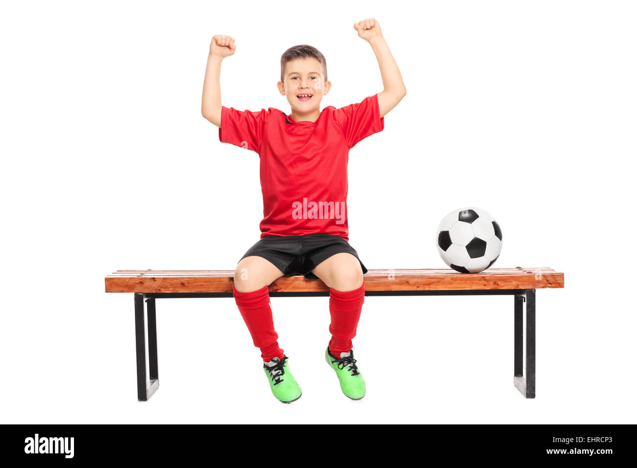 Gioiosa junior soccer player gesticolando felicità seduto su un banco di lavoro isolato su sfondo bianco Foto Stock