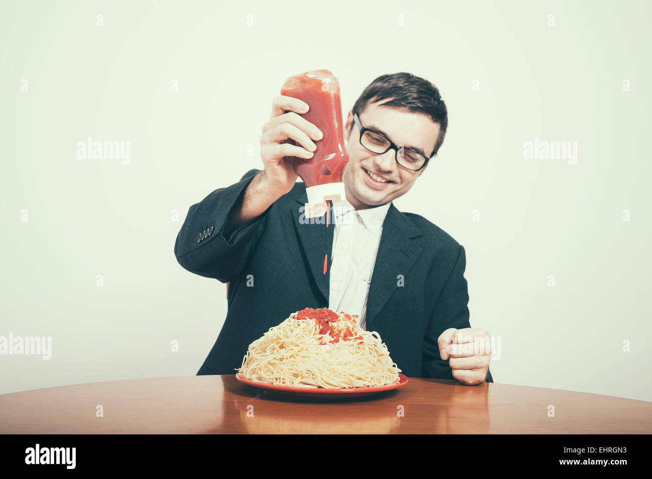 Felice il consumismo concetto. Happy businessman versando il ketchup su un enorme piatto di pasta. Foto Stock
