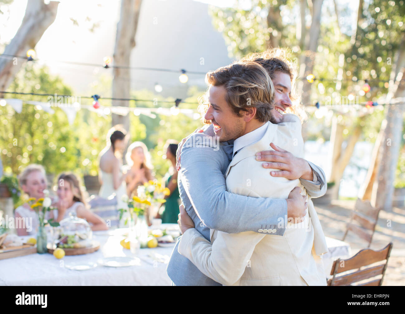 Sposo e miglior uomo abbracciando durante il ricevimento di nozze nel giardino interno Foto Stock