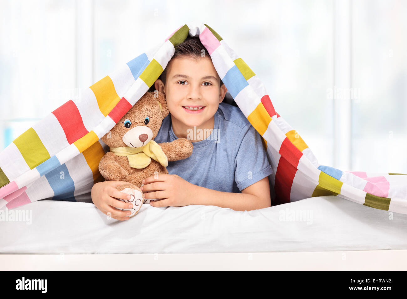 Giocoso kid tenendo un orsacchiotto sotto una coperta a casa Foto Stock