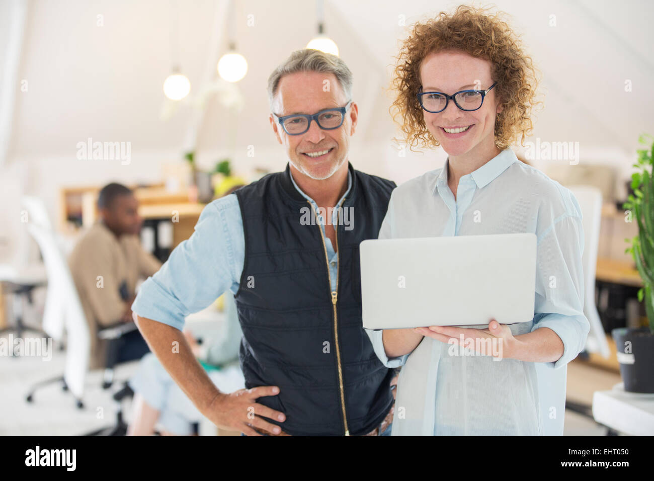Ritratto di un uomo e di una donna con il computer portatile, sorridente in ufficio Foto Stock