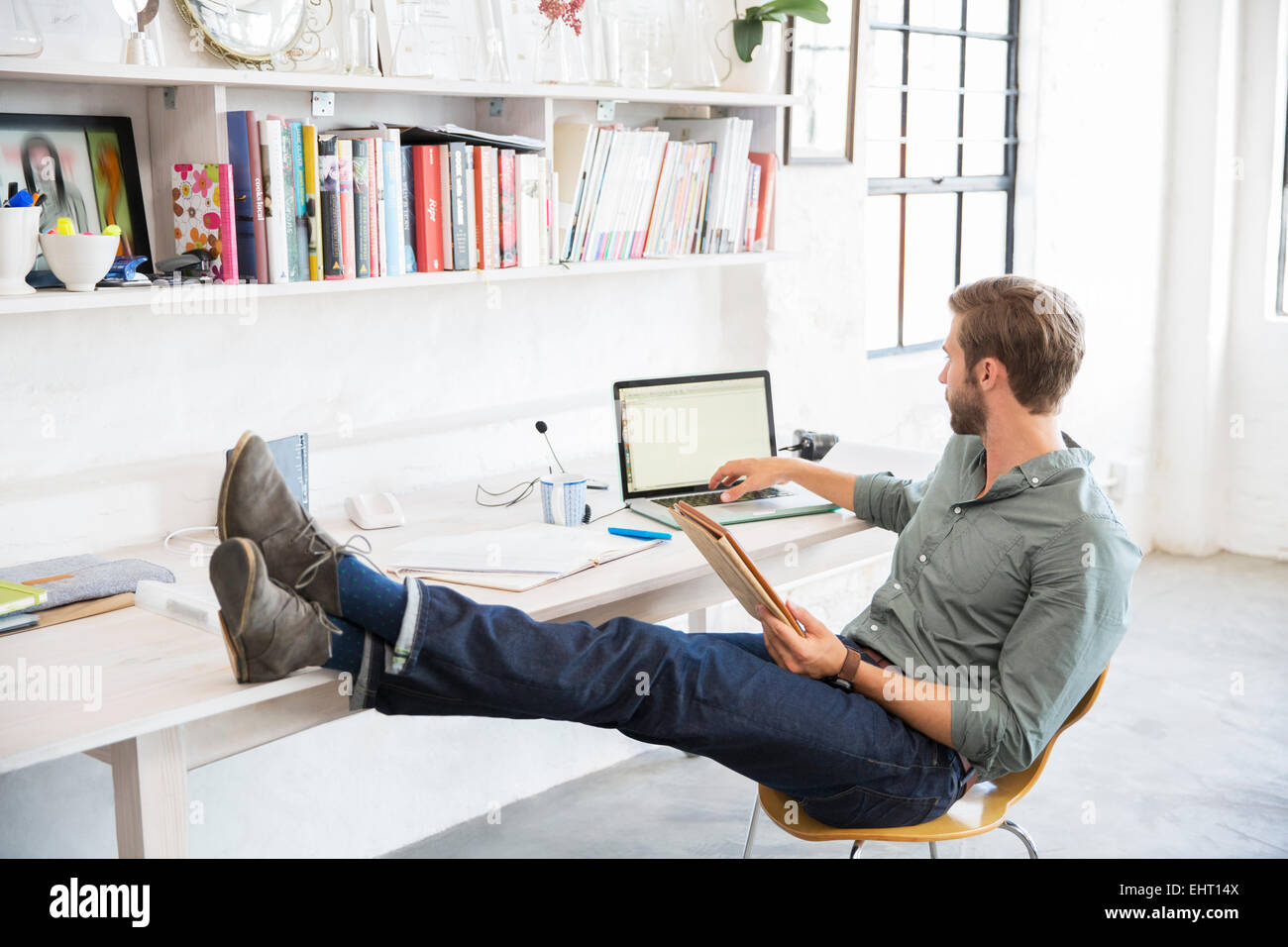 Ritratto di giovane uomo seduto con le gambe sulla scrivania che lavora con il computer portatile Foto Stock