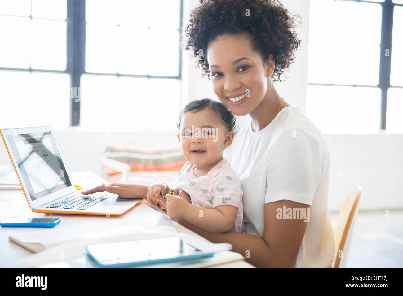 La madre lavora da casa con la figlia seduta sul suo giro Foto Stock