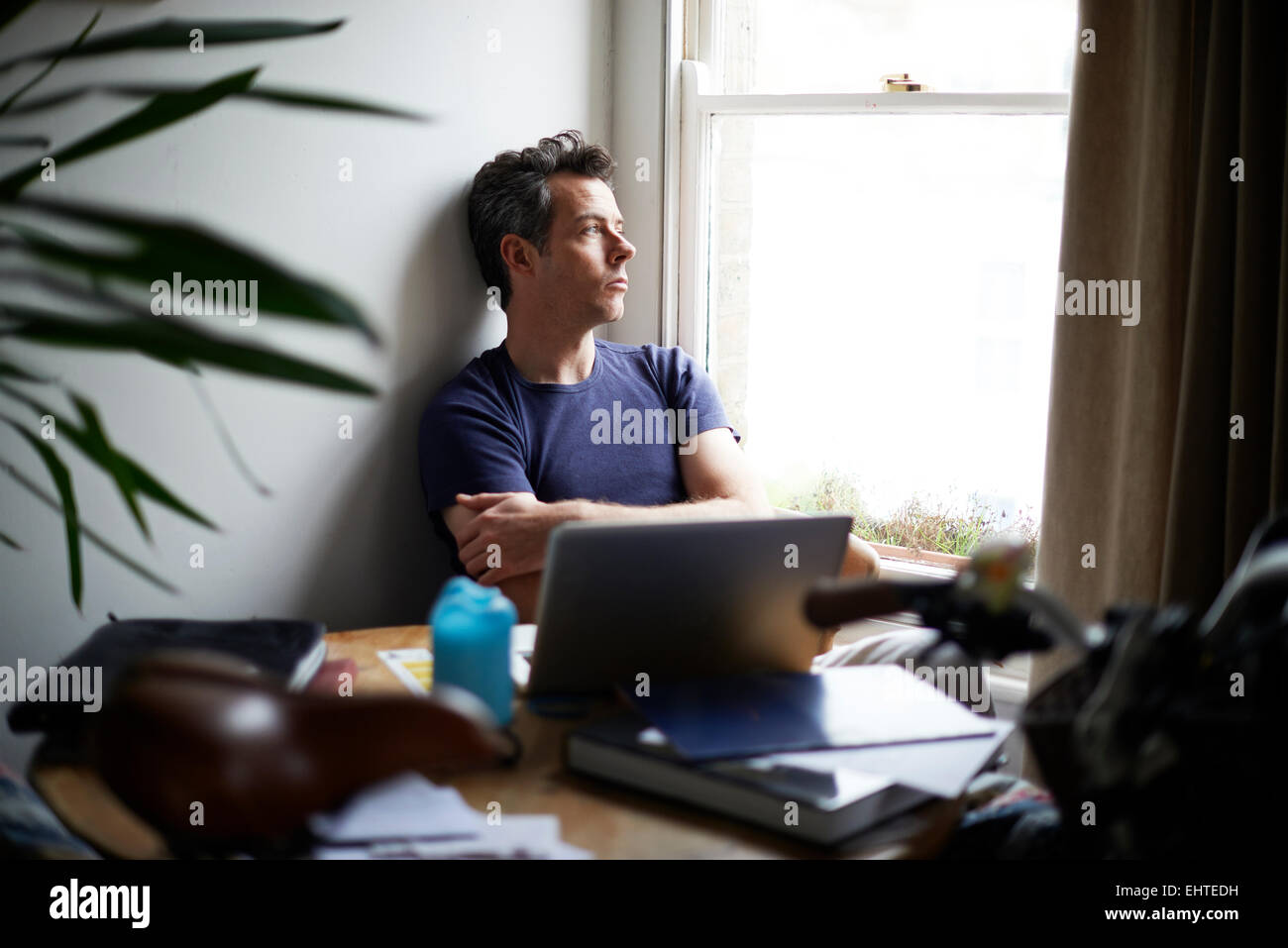 Uomo seduto al tavolo con i laptop aperti guardando attraverso la finestra Foto Stock