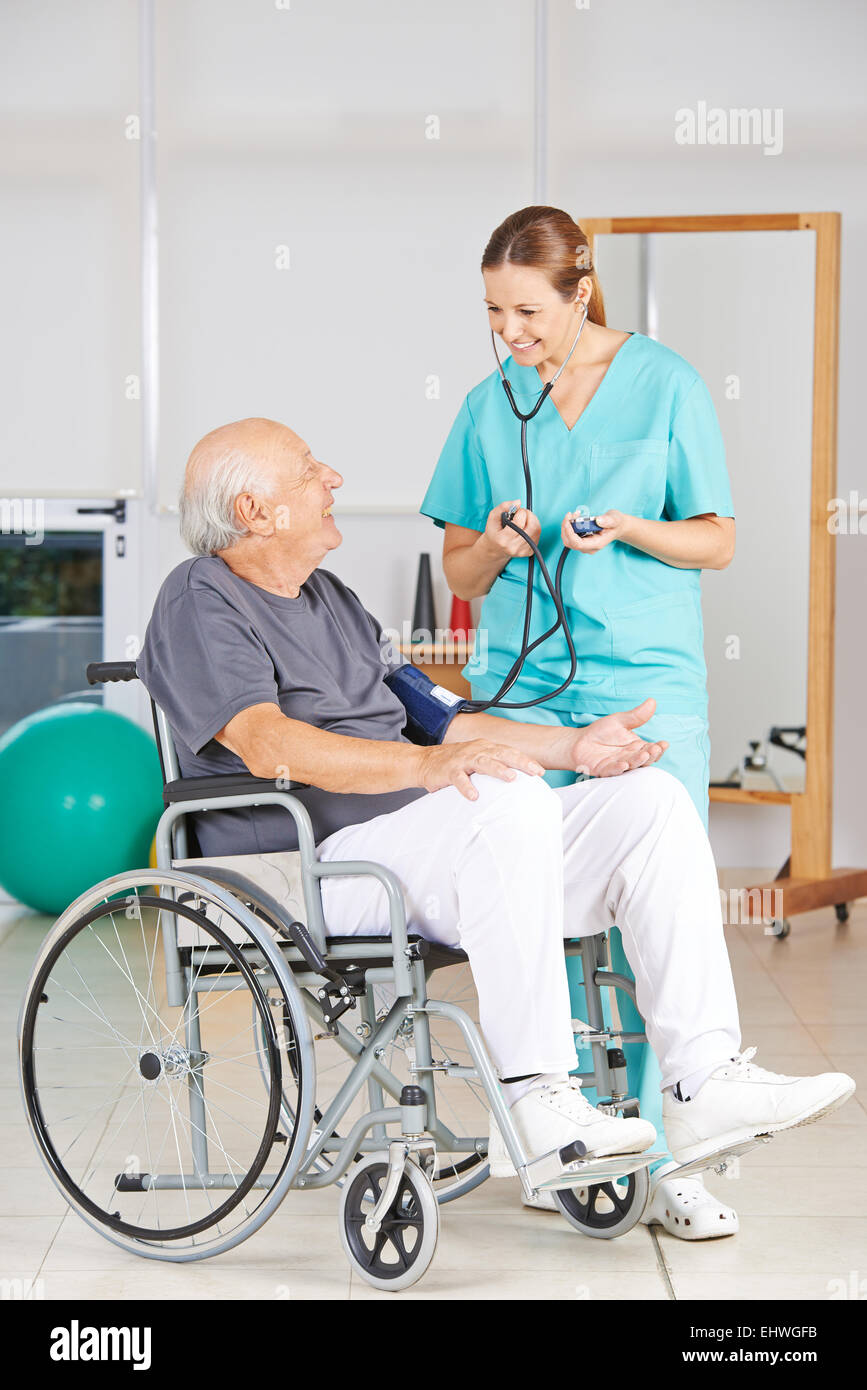 Senior uomo in sedia a rotelle come ottenere la misurazione della pressione sanguigna da infermiera geriatrica Foto Stock