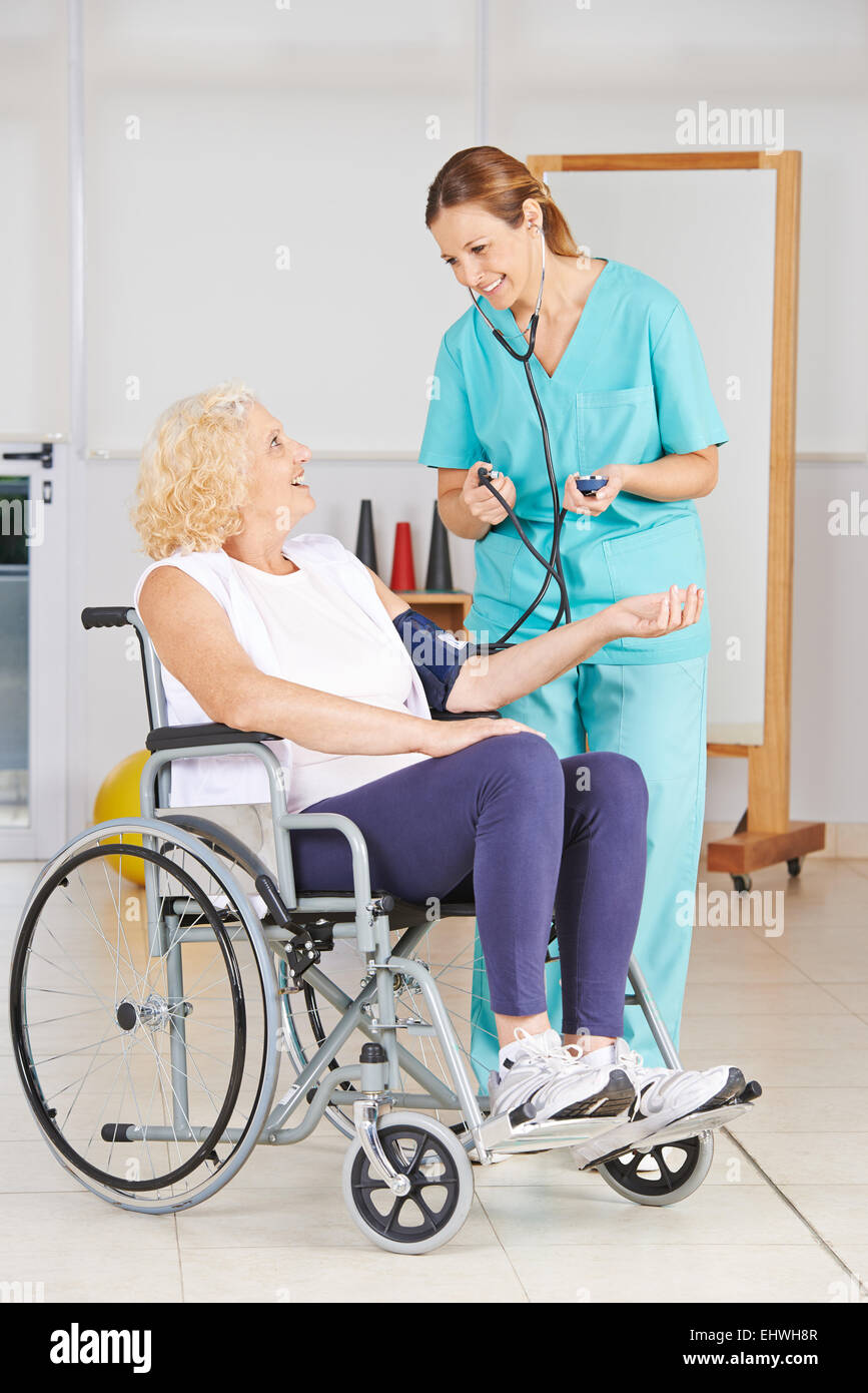 Senior donna in sedia a rotelle come ottenere la misurazione della pressione sanguigna in una casa di cura Foto Stock