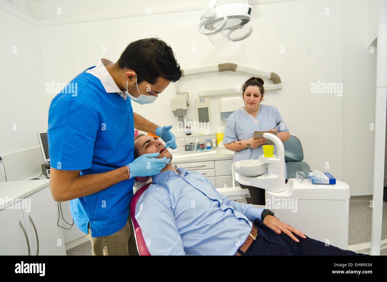Dentista esaminare il paziente di sesso maschile in bocca con grande concentrazione, mentre l'infermiera prendendo appunti Foto Stock