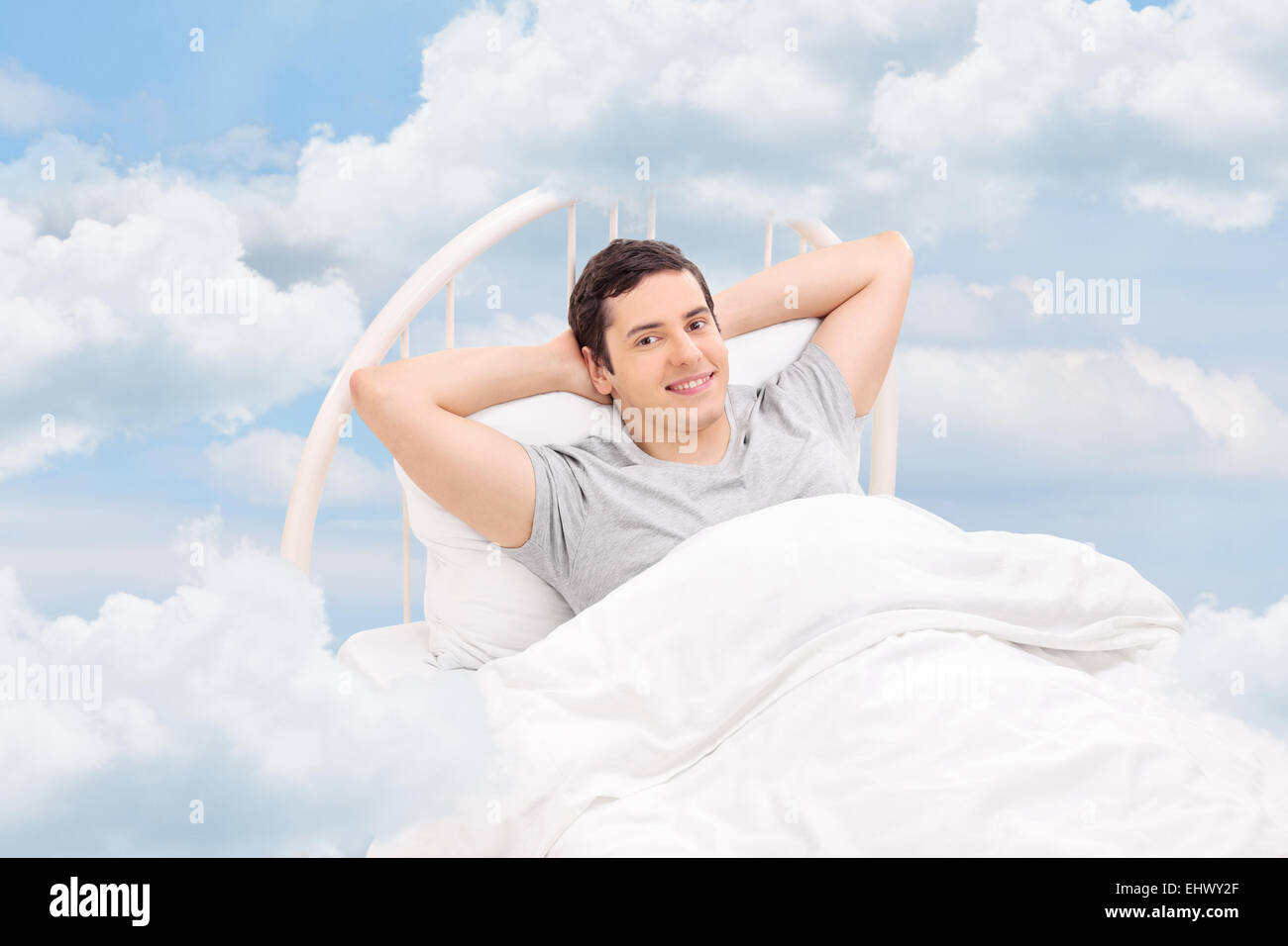 Giovane uomo rilassante su un comodo letto tra le nuvole Foto Stock