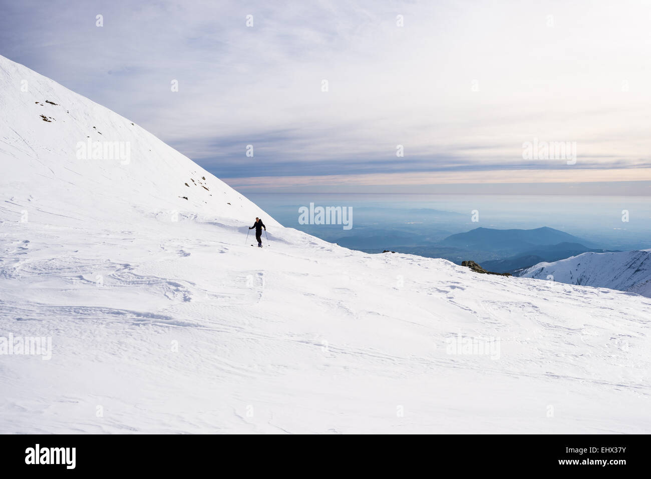 Paese indietro sciatore escursionismo in salita su pendio nevoso con vista panoramica in background. Concetto di conquista di avversità. Foto Stock