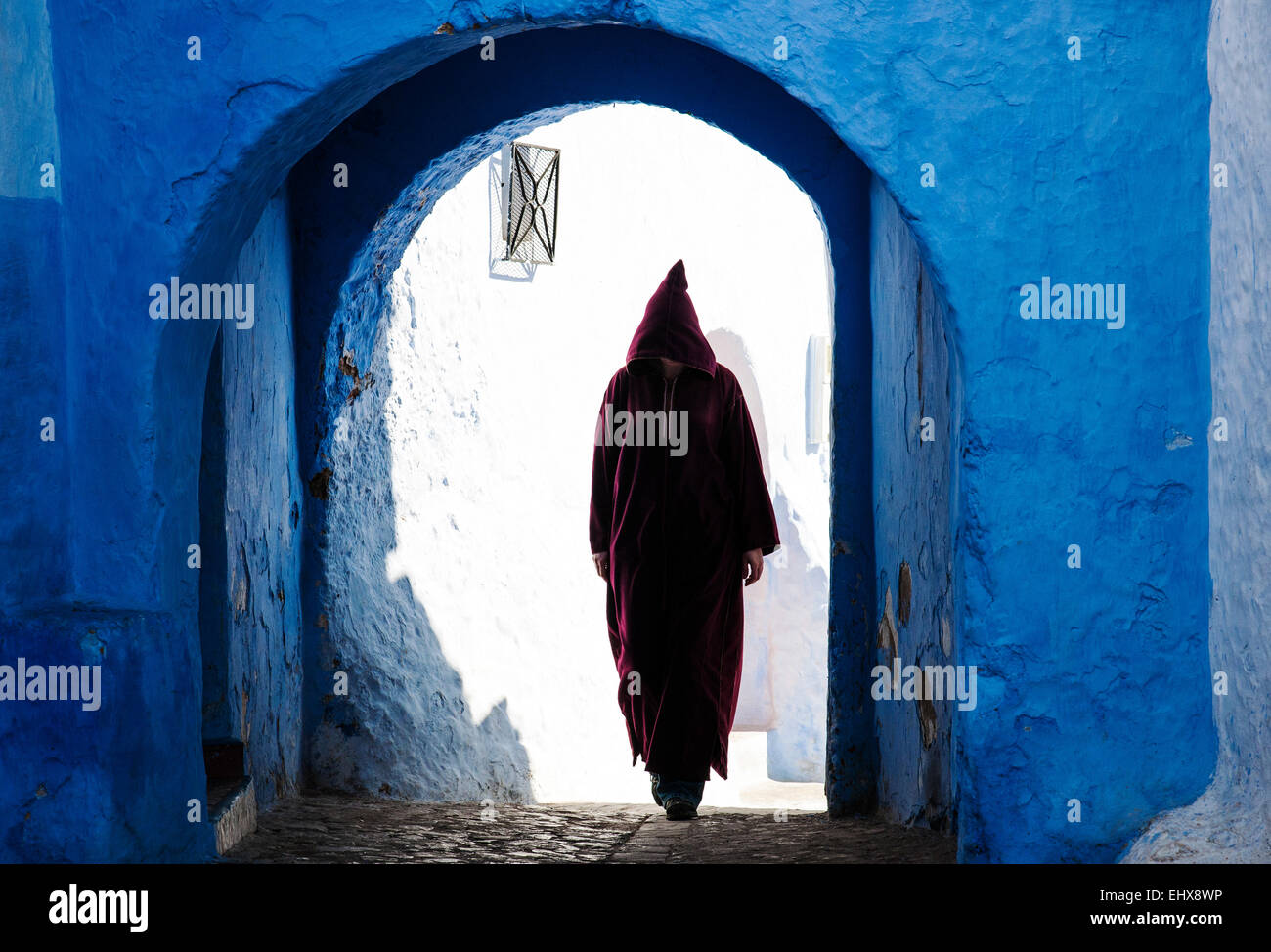 Una donna in djellaba tradizionale a piedi il blu-lavato strade di Chefchaouen, Marocco Foto Stock