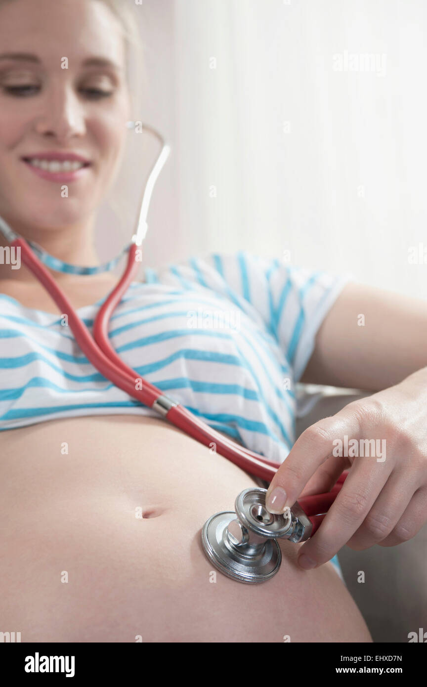 Donna incinta tenendo uno stetoscopio stomaco Foto Stock