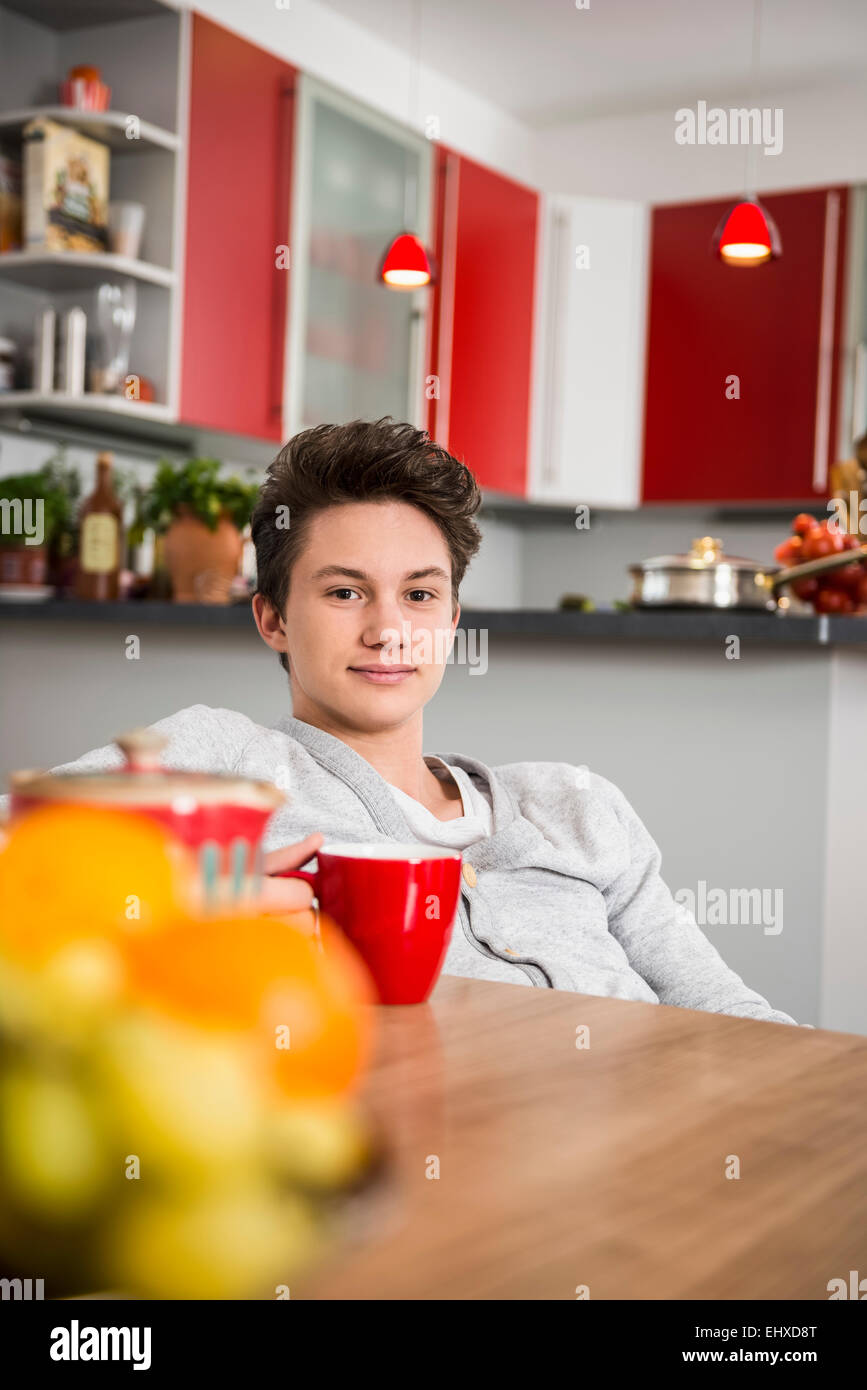 Giovane uomo seduto con un bicchiere in mano al tavolo della cucina, Monaco di Baviera, Germania Foto Stock