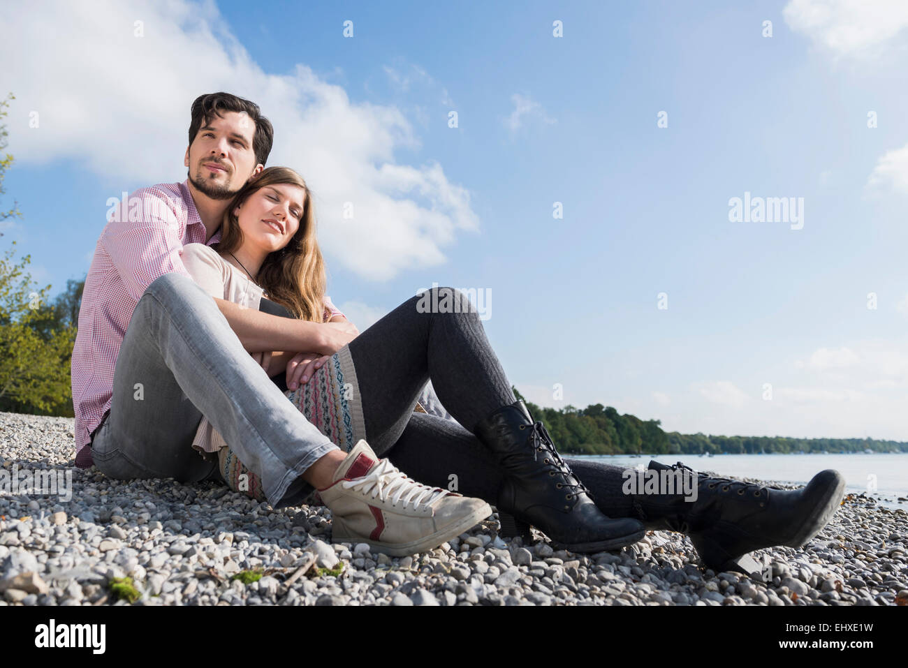 Giovane seduto abbracciando lake shore felice Foto Stock